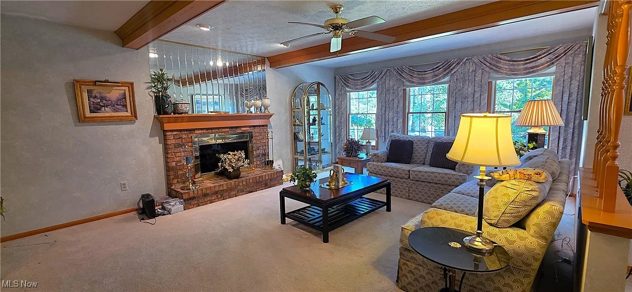 Family room featuring a beamed ceiling, a fireplace, and a ceiling fan