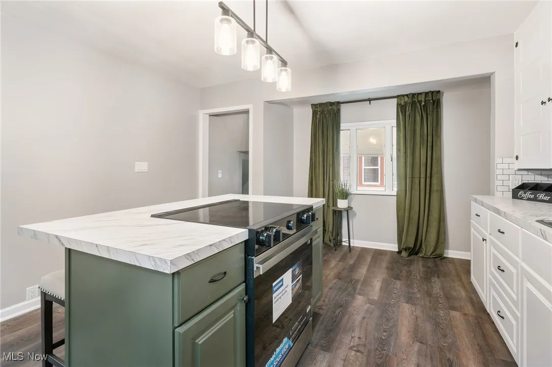 Kitchen with black range with electric stovetop, dark wood-style floors, a kitchen island, green cabinetry, and hanging light fixtures