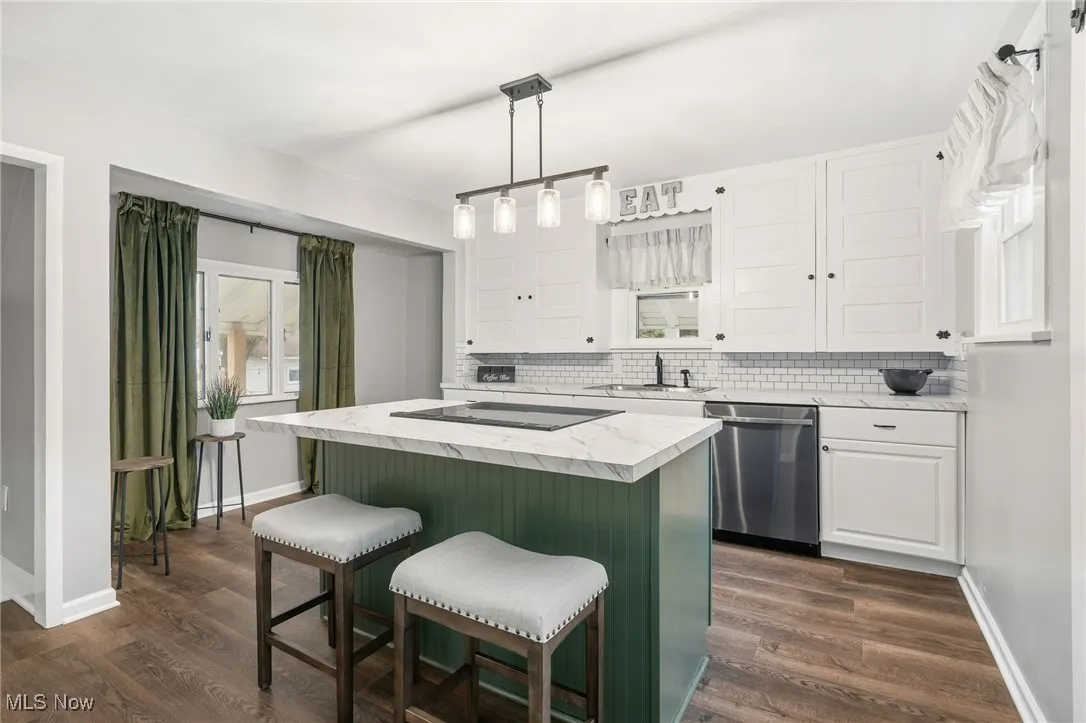 Kitchen with light countertops, white cabinets, a center island, decorative light fixtures, and stainless steel dishwasher