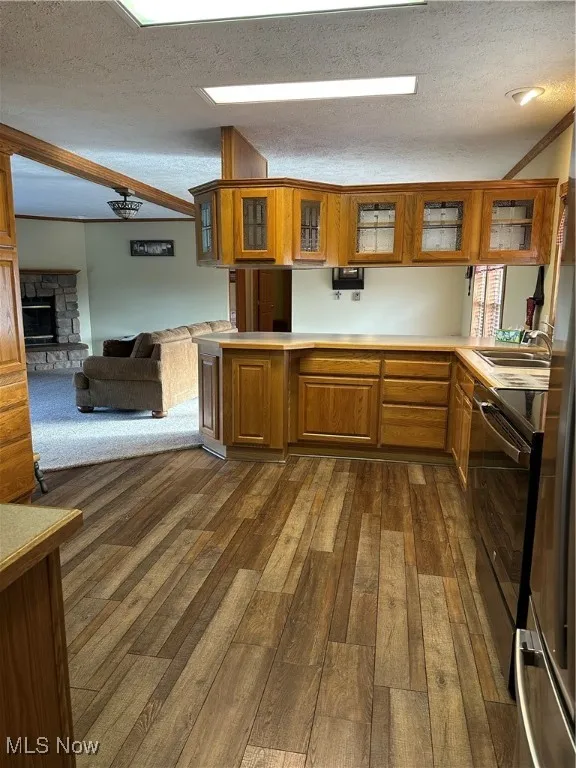 Kitchen with glass insert cabinets, a textured ceiling, brown cabinets, light countertops, and a stone fireplace and LVT flooring.