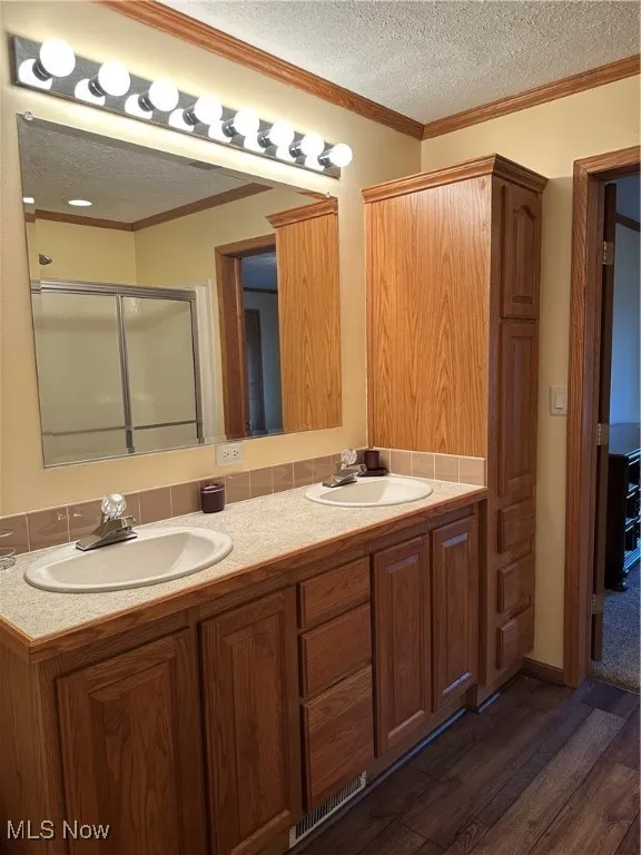 Master bath with crown molding, a textured ceiling, double vanity, dark wood-style flooring, and a stall shower