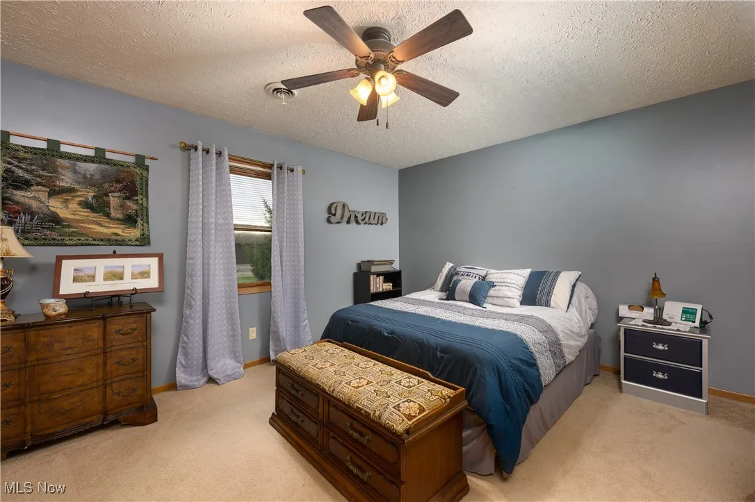 Bedroom with a textured ceiling, light colored carpet, and a ceiling fan