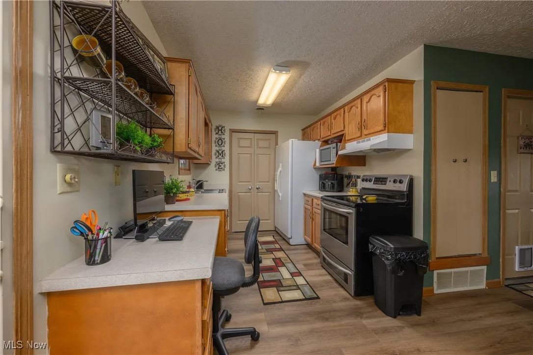 Kitchen featuring appliances with stainless steel finishes, light countertops, a textured ceiling, light wood finished floors, and brown cabinets