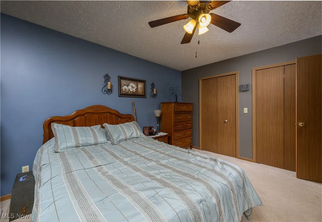 Bedroom with multiple closets, carpet flooring, ceiling fan, and a textured ceiling