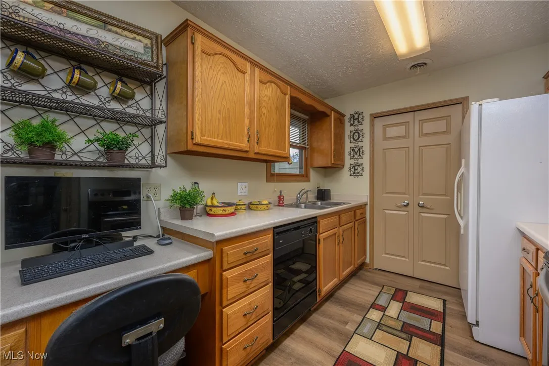 Kitchen with light countertops, freestanding refrigerator, light wood-style flooring, a textured ceiling, and dishwasher