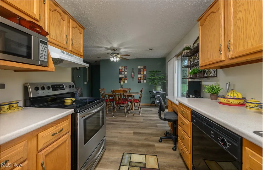 Kitchen featuring stainless steel appliances, under cabinet range hood, light wood finished floors, light countertops, and a textured ceiling
