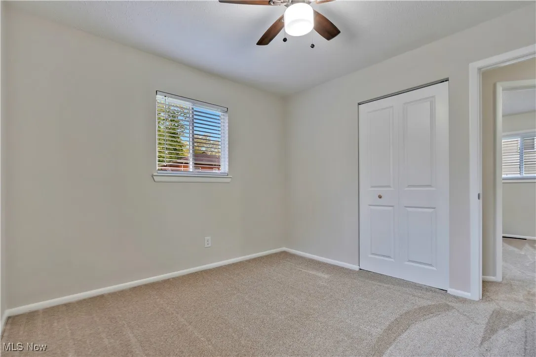 Unfurnished bedroom featuring light carpet, multiple windows, a closet, and a ceiling fan