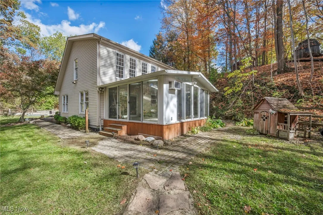 Back of house with a sunroom, a lawn, and a shed