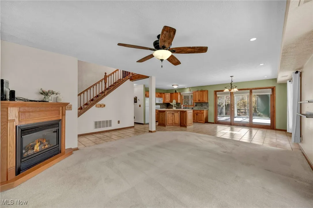 Unfurnished living room with light tile patterned flooring, light carpet, a glass covered fireplace, a chandelier, and recessed lighting