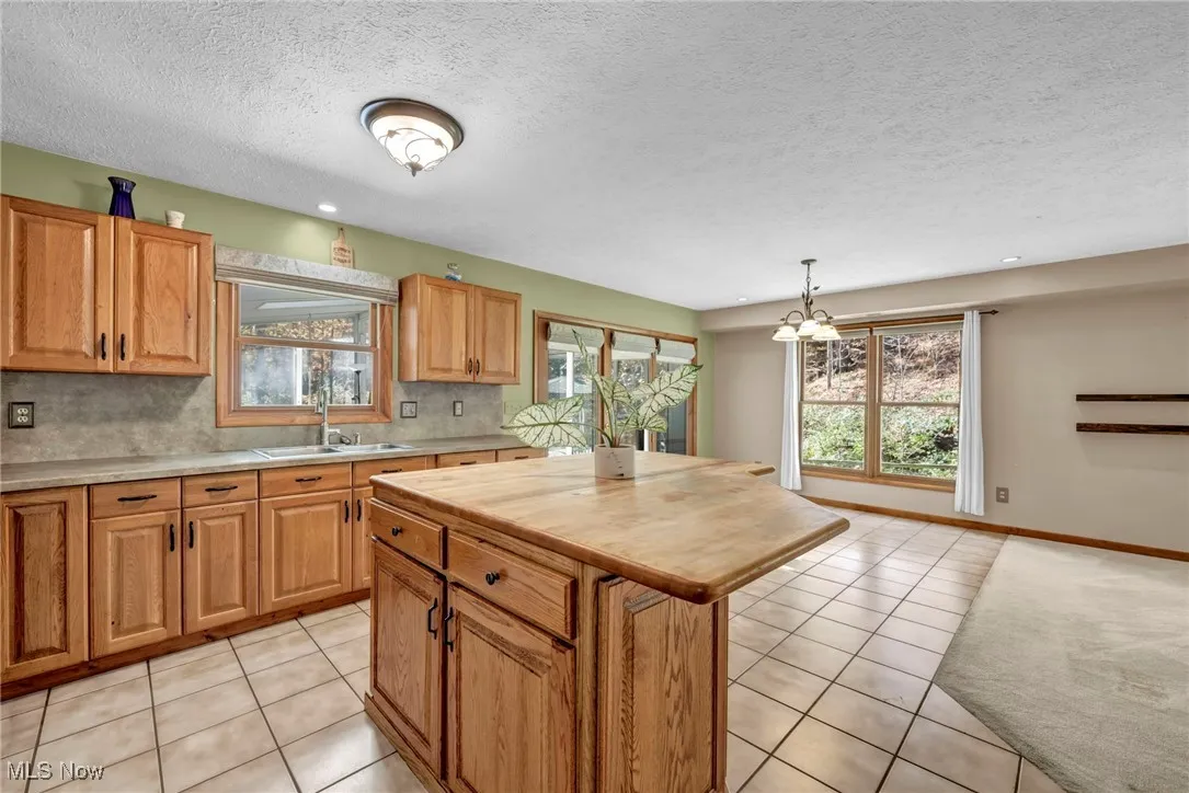 Kitchen featuring light tile patterned flooring, decorative backsplash, pendant lighting, a center island, and a textured ceiling