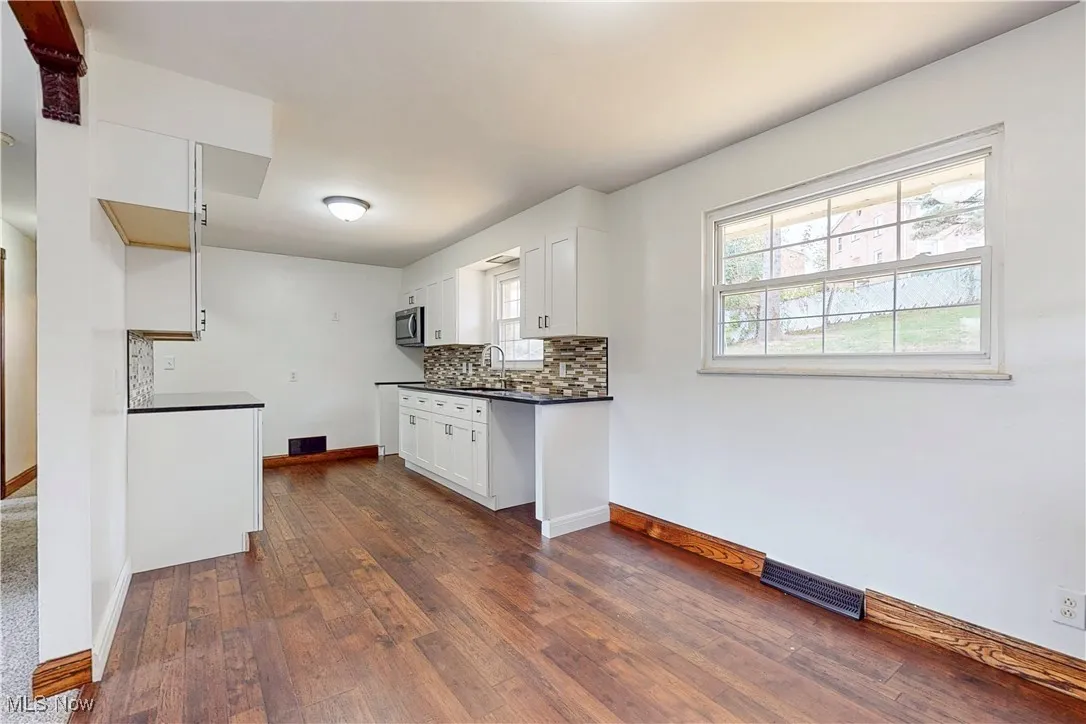 Kitchen featuring dark countertops, backsplash, plenty of natural light, and white cabinetry