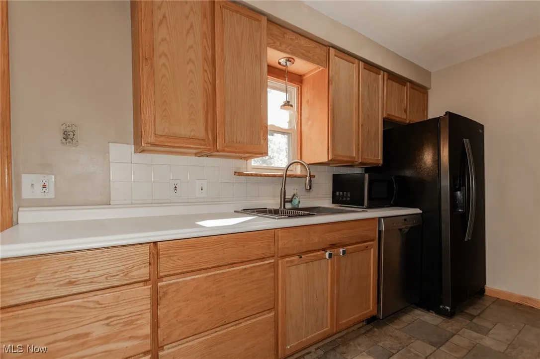Kitchen with light countertops, decorative backsplash, black appliances, dark stone finish flooring, and pendant lighting