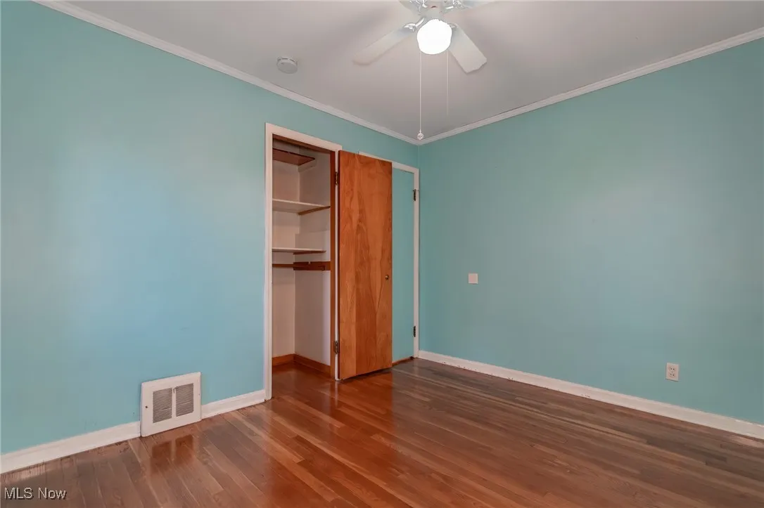 Unfurnished bedroom featuring dark wood-type flooring, ornamental molding, a closet, and a ceiling fan