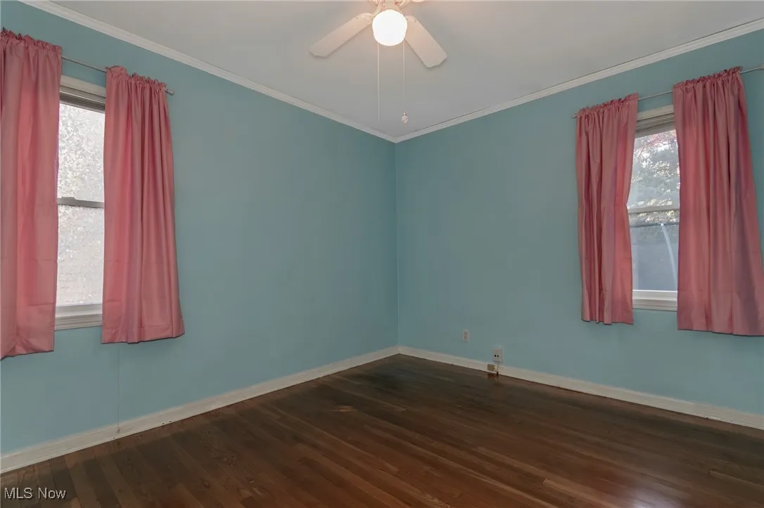 Spare room with dark wood-style flooring, ornamental molding, and a ceiling fan