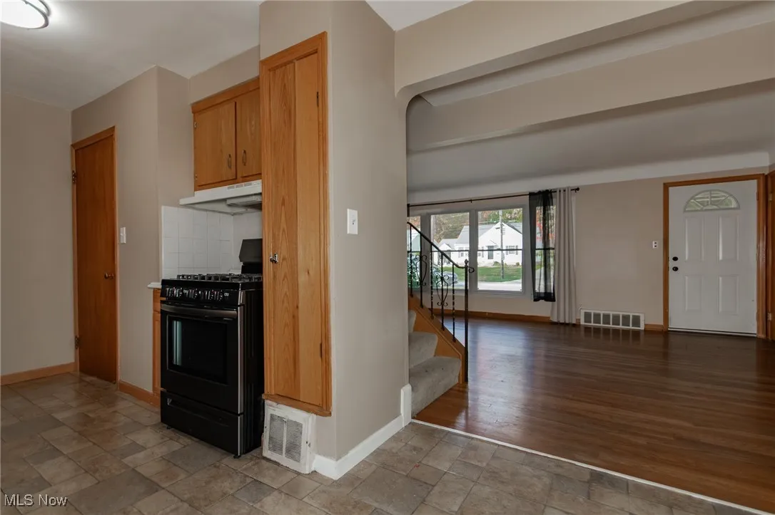 Kitchen featuring gas stove, stone tile floors, under cabinet range hood, tasteful backsplash, and brown cabinetry
