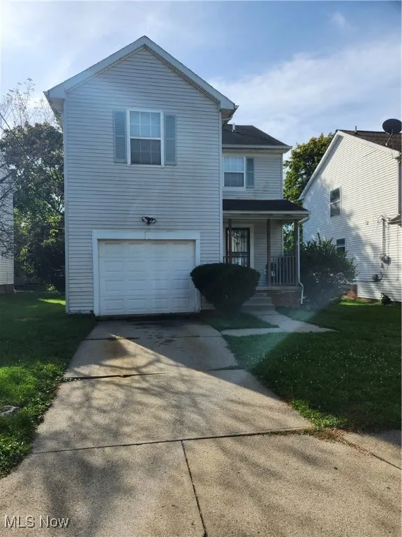Traditional-style home featuring a porch, driveway, a front yard, and an attached garage