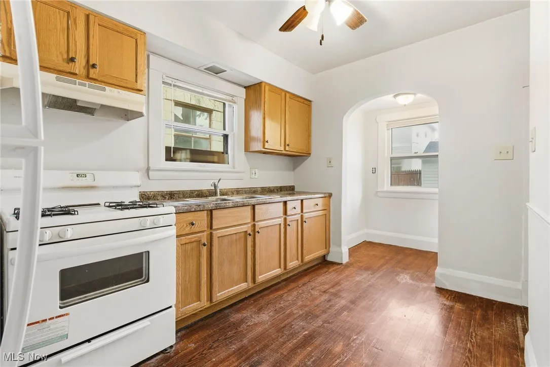 Kitchen with white range with gas cooktop, under cabinet range hood, dark wood finished floors, and plenty of natural light
