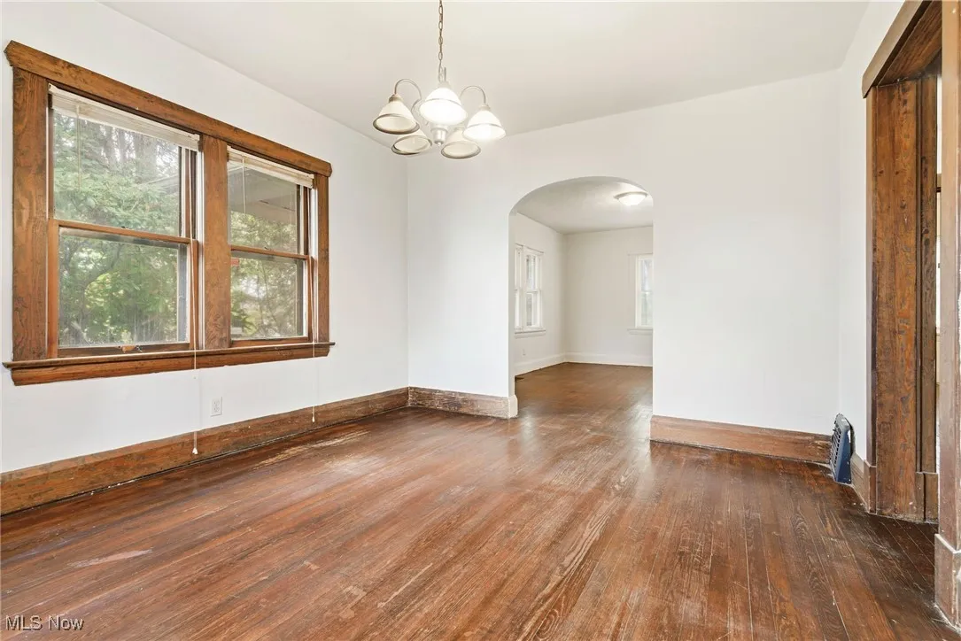 Spare room with dark wood finished floors, arched walkways, and a chandelier