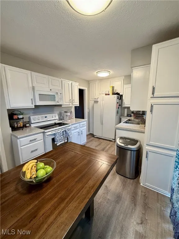 Kitchen with white cabinetry, white appliances, a textured ceiling, and light wood-style flooring
