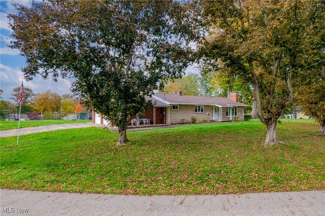 Ranch-style home with a chimney, concrete driveway, a front yard, a porch, and a garage