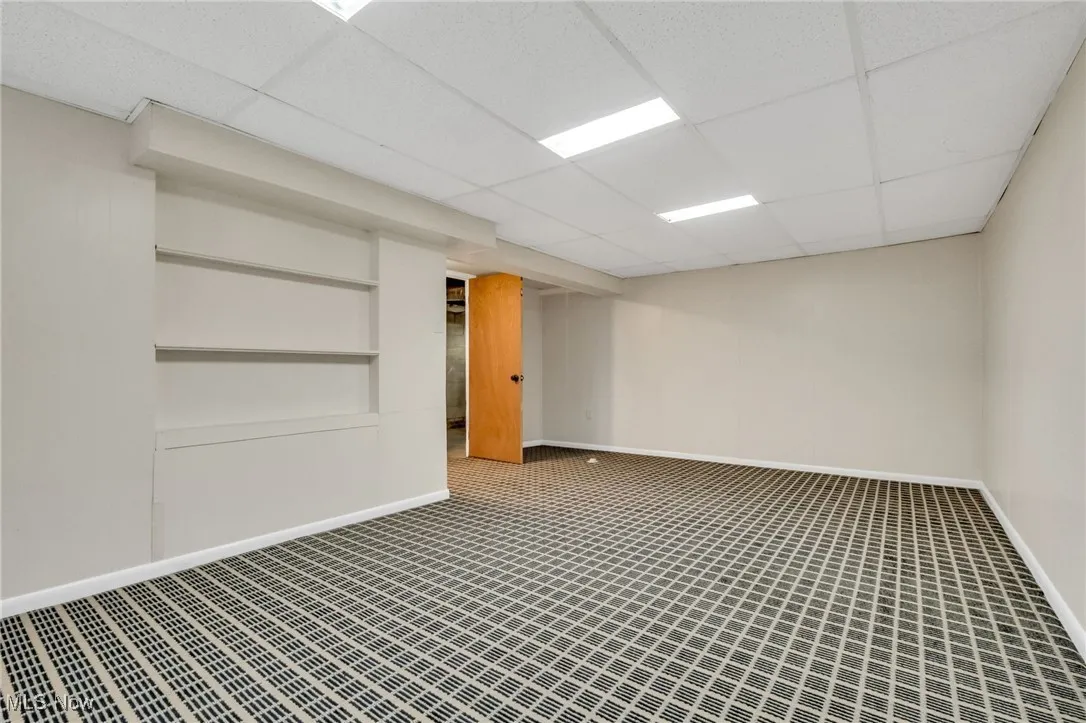 Carpeted empty room featuring a drop ceiling and built in shelves