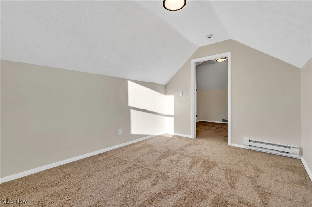 Bonus room with carpet flooring, baseboard heating, vaulted ceiling, and a textured ceiling