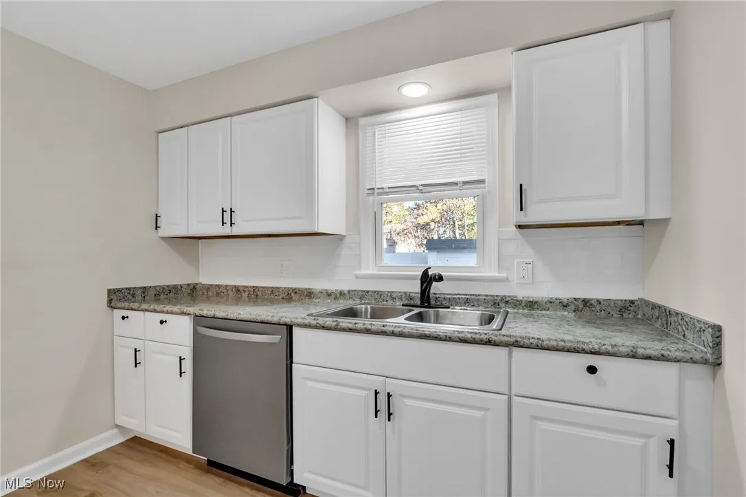 Kitchen with stainless steel dishwasher, white cabinets, light wood-type flooring, and tasteful backsplash