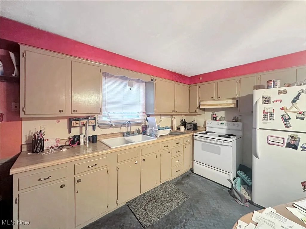 Kitchen with white appliances, light countertops, cream cabinets, and under cabinet range hood