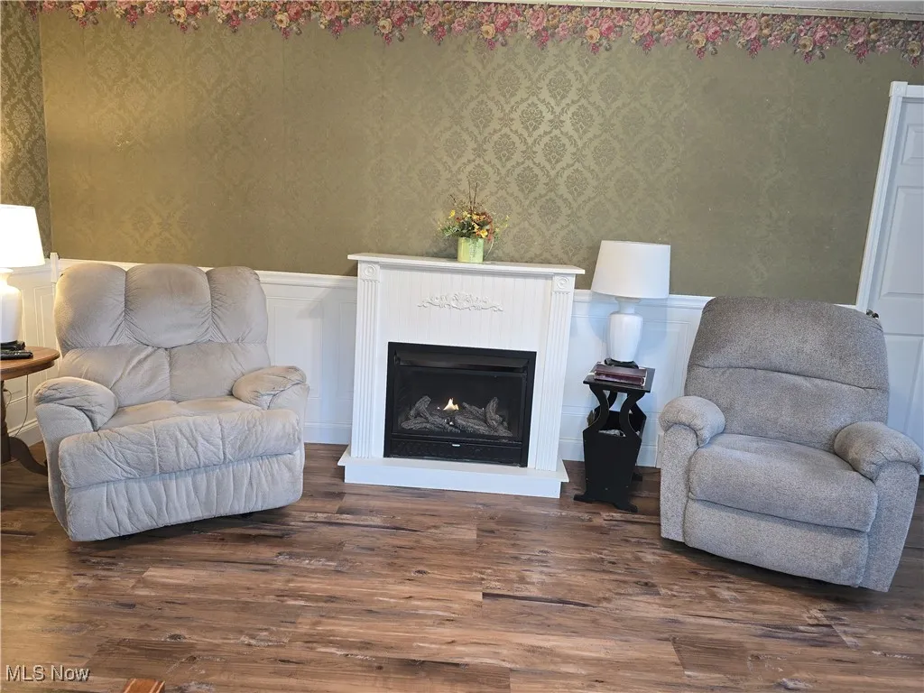 Sitting room featuring wainscoting, a lit fireplace, dark wood-type flooring, a decorative wall, and wallpapered walls