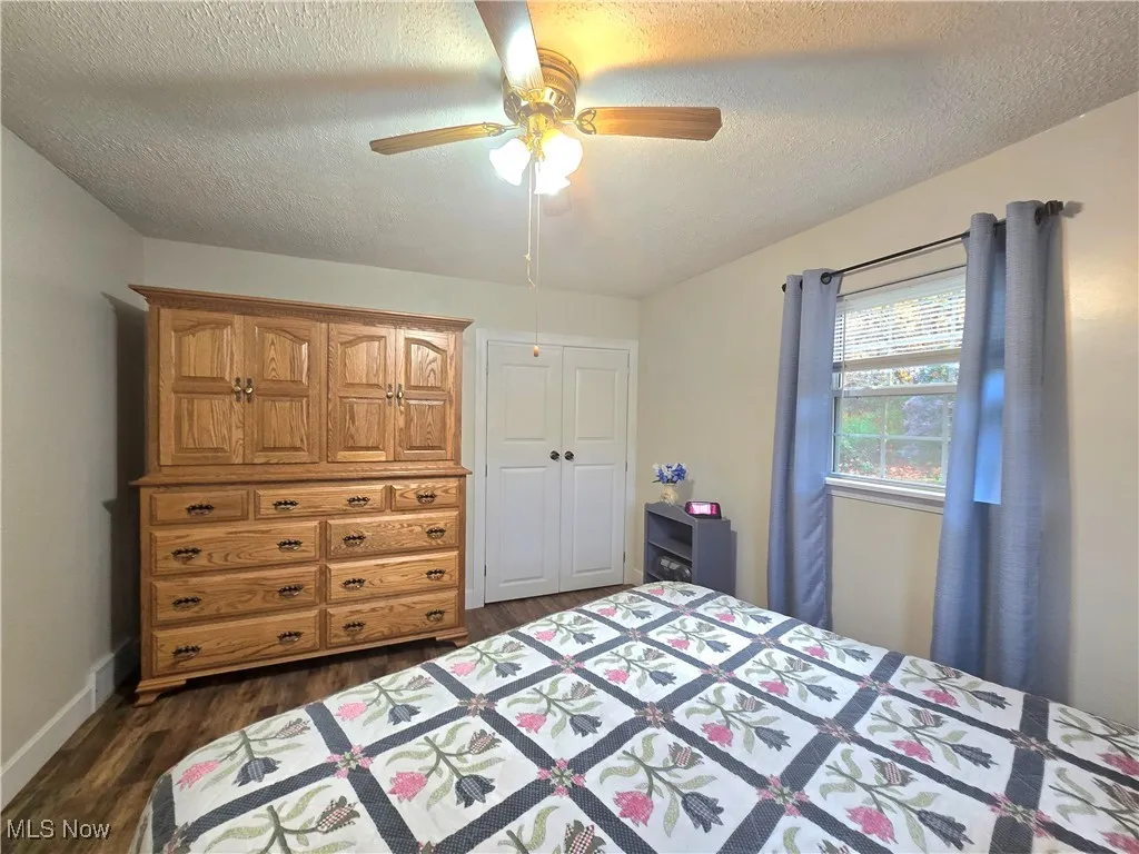 Bedroom with a textured ceiling, dark wood-style flooring, a ceiling fan, and a closet