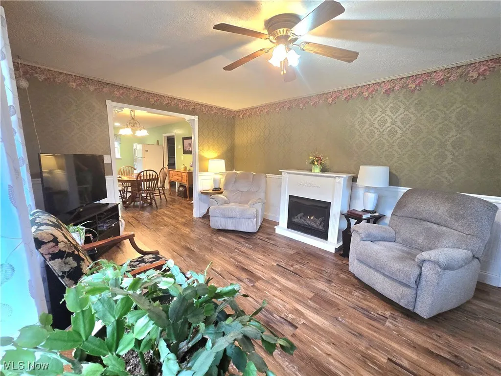 Living area featuring dark wood finished floors, wallpapered walls, a textured ceiling, a fireplace, and a chandelier