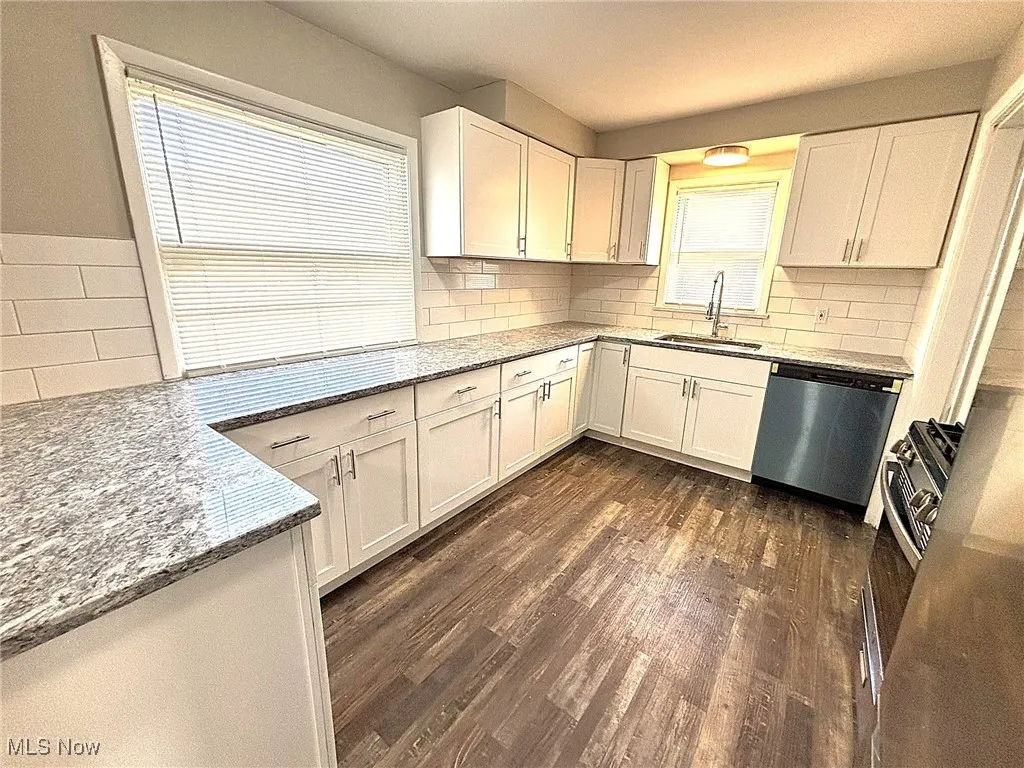 Kitchen featuring light stone countertops, decorative backsplash, dark wood-style floors, and appliances with stainless steel finishes