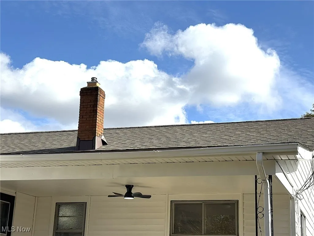 Exterior view of a shingled roof, a chimney, and ceiling fan