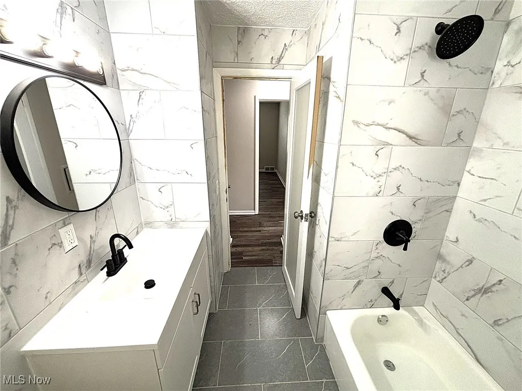 Bathroom with tile walls, shower / bath combination, vanity, a textured ceiling, and dark tile patterned floors