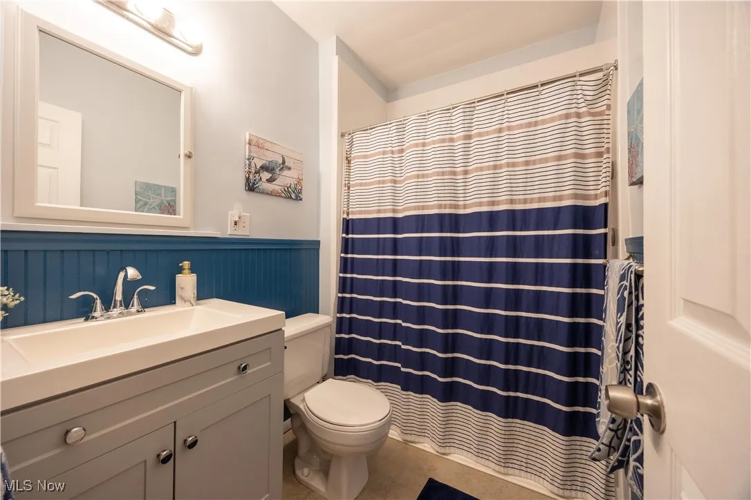 Full bath with vanity, curtained shower, tile patterned flooring, and a wainscoted wall
