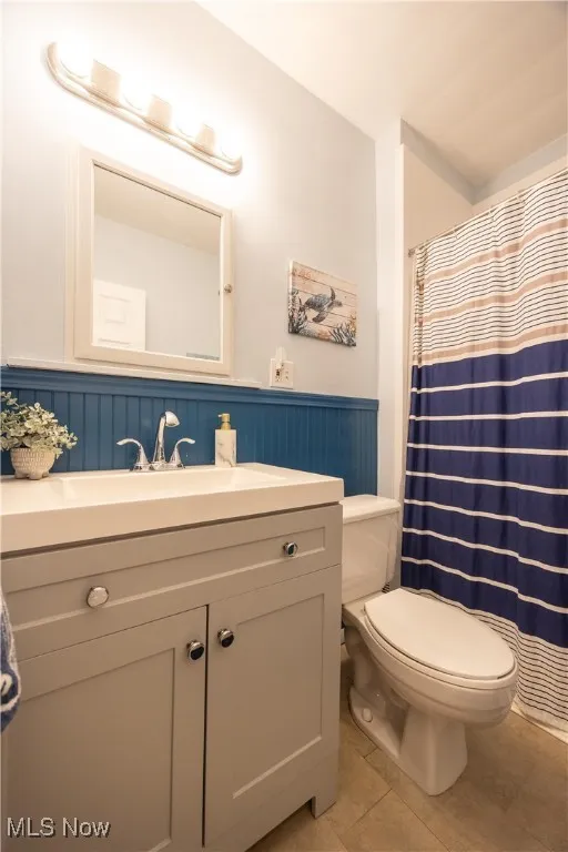 Bathroom featuring a shower with shower curtain, vanity, light tile patterned flooring, and wainscoting