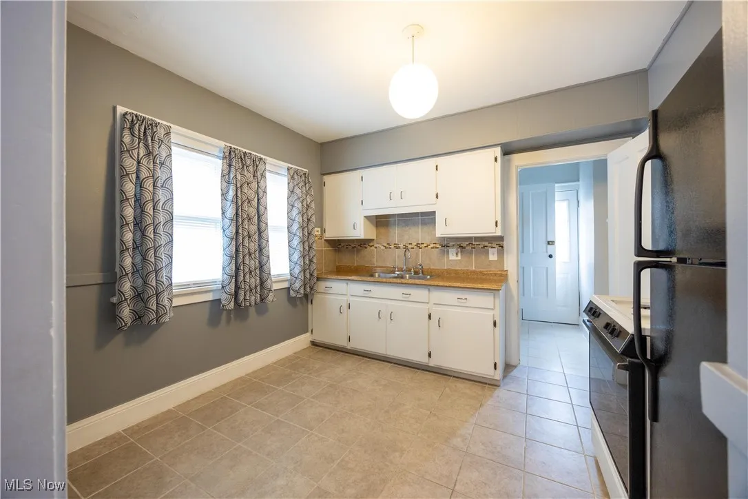 Kitchen featuring tasteful backsplash, black appliances, light countertops, and white cabinets
