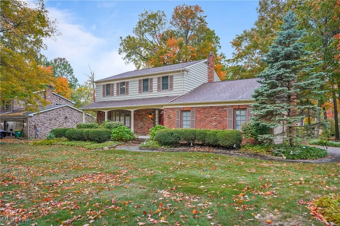 View of front of home with a front lawn, a chimney, covered porch, brick siding