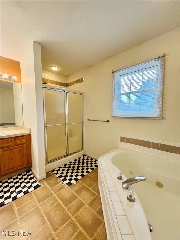 Full bath featuring a tub with jets, a stall shower, vanity, and light tile patterned floors