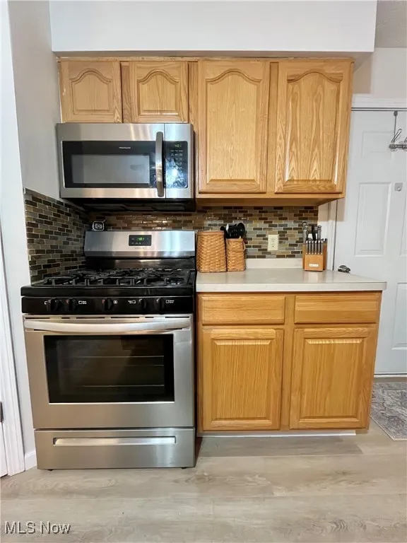 Kitchen with stainless steel appliances, light countertops, backsplash, and light wood-style floors