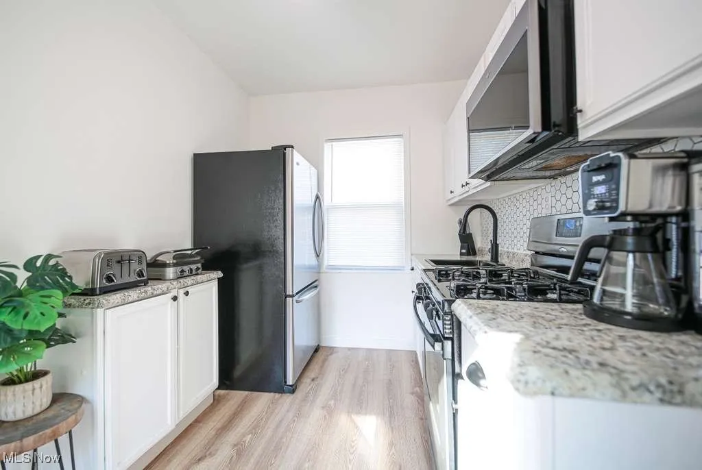 Kitchen with white cabinetry, stainless steel appliances, light wood-style flooring, and backsplash