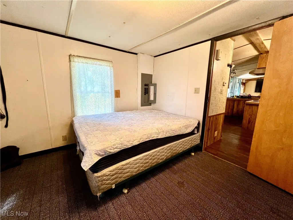 Bedroom with multiple windows, electric panel, wooden walls, dark carpet, and a wainscoted wall