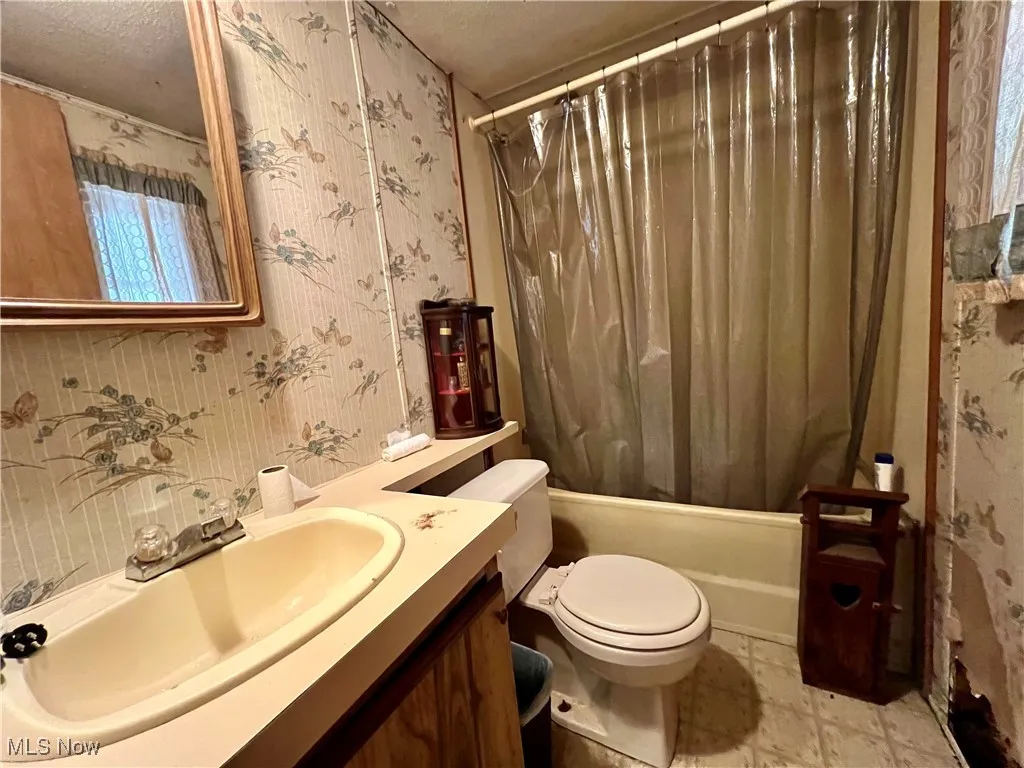 Bathroom featuring wallpapered walls, vanity, shower / bath combo with shower curtain, and a textured ceiling