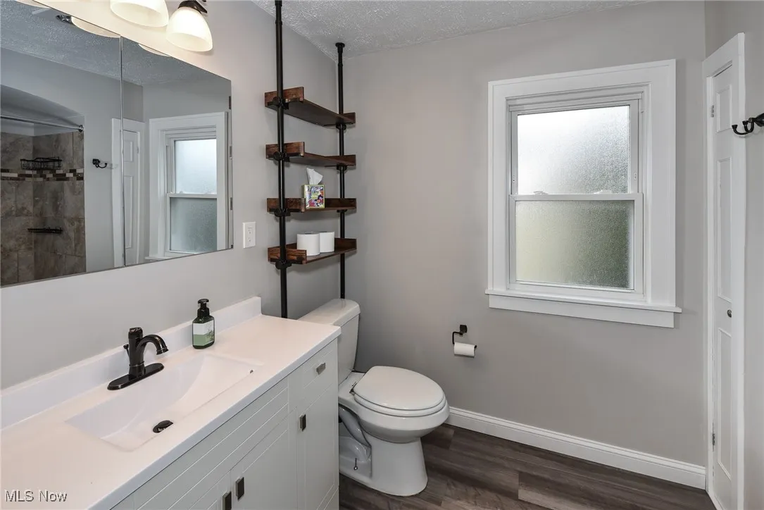 Full bath featuring a textured ceiling, dark wood finished floors, vanity, and a tile shower