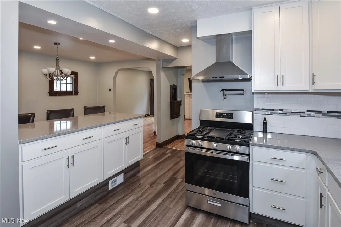 Kitchen featuring stainless steel range with gas cooktop, white cabinets, wall chimney exhaust hood, and recessed lighting
