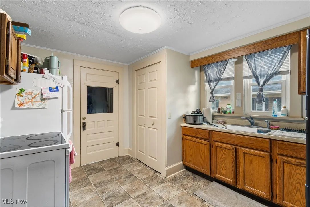 Kitchen featuring range with electric cooktop, a textured ceiling, brown cabinets, light countertops, and freestanding refrigerator