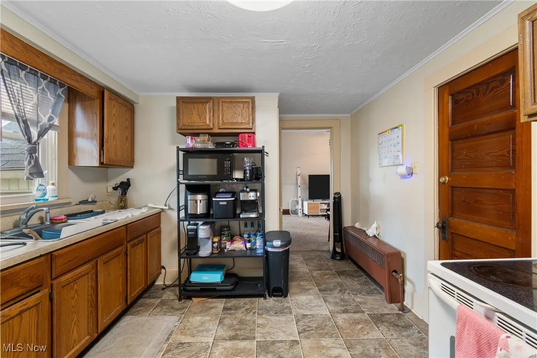 Kitchen with brown cabinets, light countertops, a textured ceiling, ornamental molding, and radiator heating unit