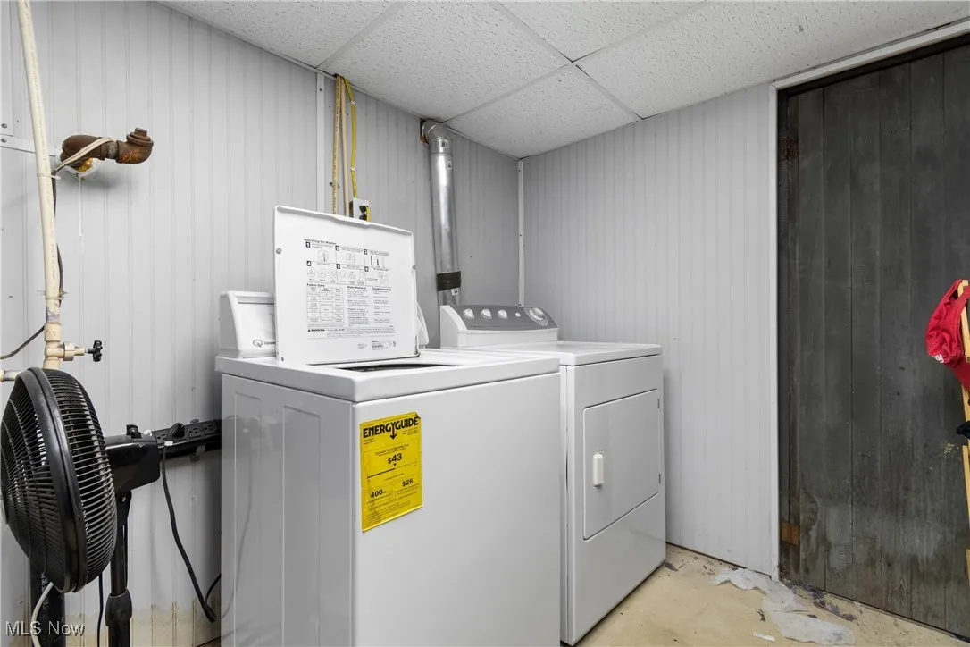 Laundry area featuring washing machine and dryer, a drop ceiling, and wood walls