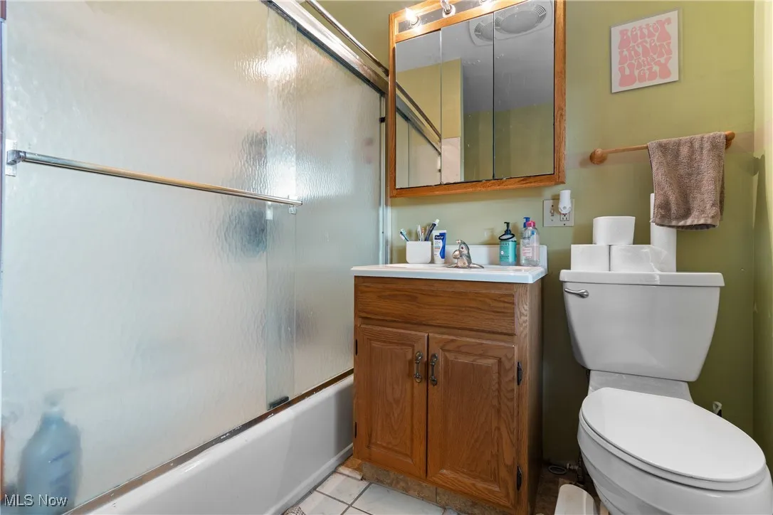 Bathroom featuring vanity, light tile patterned floors, and combined bath / shower with glass door