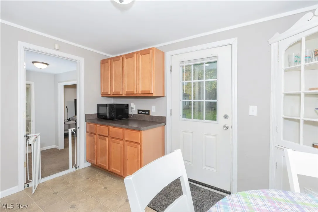Kitchen with dark countertops, black microwave, crown molding, and light tile patterned floors